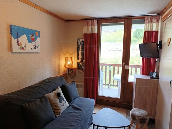 A cozy room with a sofa, a small table, a TV, and a window with curtains.
