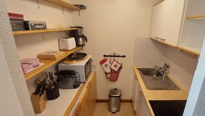 A compact kitchen with wooden shelves, a toaster, a coffee maker, a sink, and a trash bin. - Paradiski closed to the slopes vallandry (LANDRY)