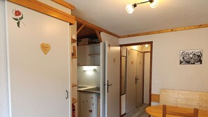 A compact kitchen with a refrigerator, a sink, and a wooden stool. There is a dining table with a bench and a wall-mounted light fixture. - Paradiski closed to the slopes vallandry (LANDRY)
