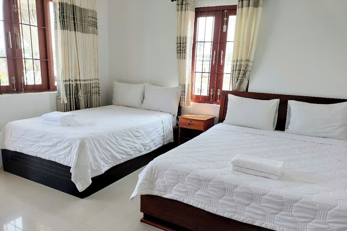 A hotel room with two single beds, a wooden headboard, a nightstand, and a window with curtains.