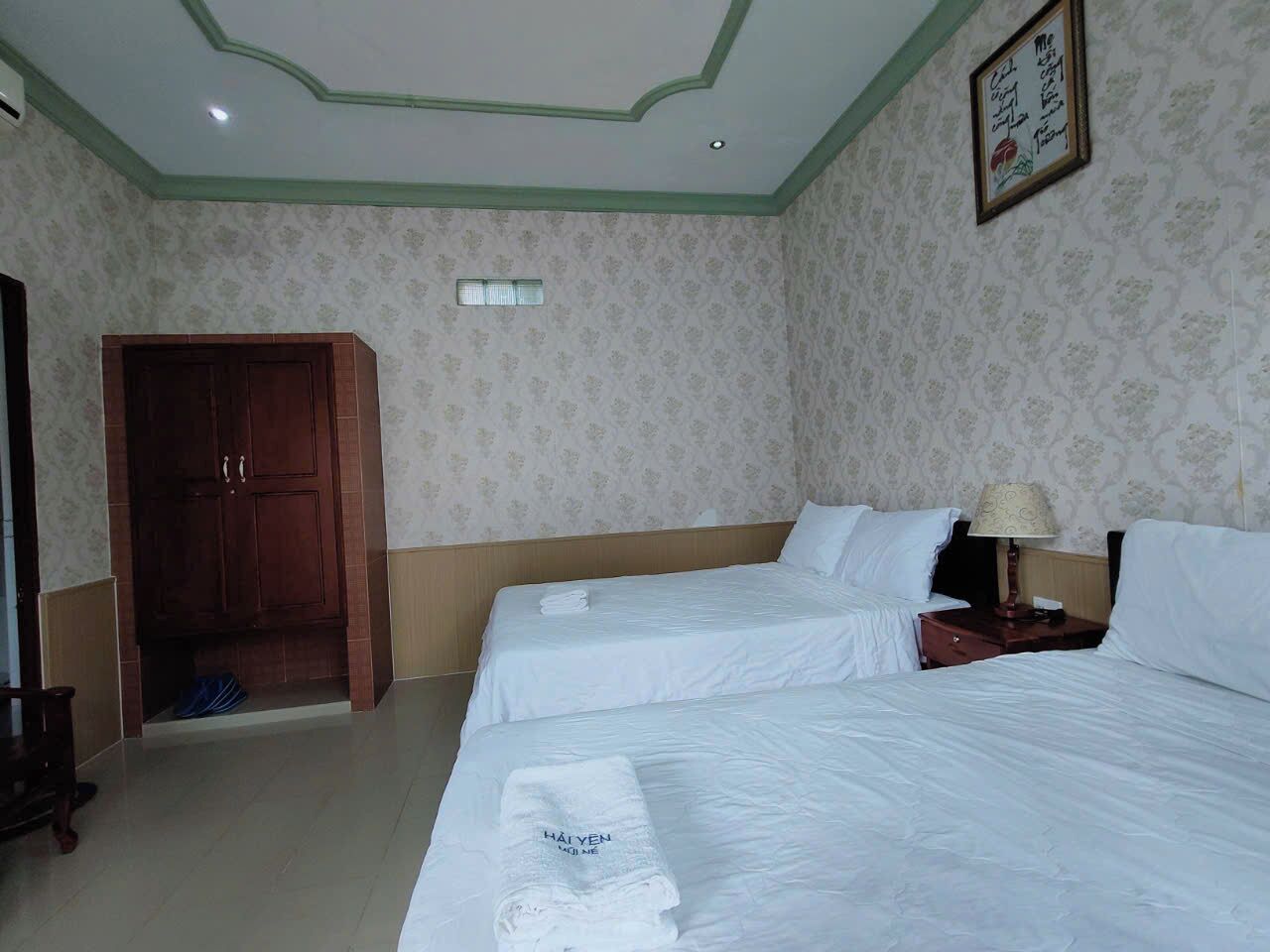 A hotel room with two beds, a wooden wardrobe, a door, and a wall-mounted lamp.
