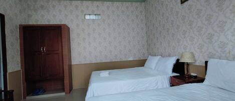 A hotel room with two beds, a wooden wardrobe, a door, and a wall-mounted lamp.