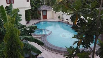 Una piscina rodeada de plantas tropicales y un pequeño edificio con una puerta roja.
