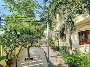 A pathway lined with trees and potted plants, leading to a building with a number '102' sign. - Min's Homestay (Mui Ne)