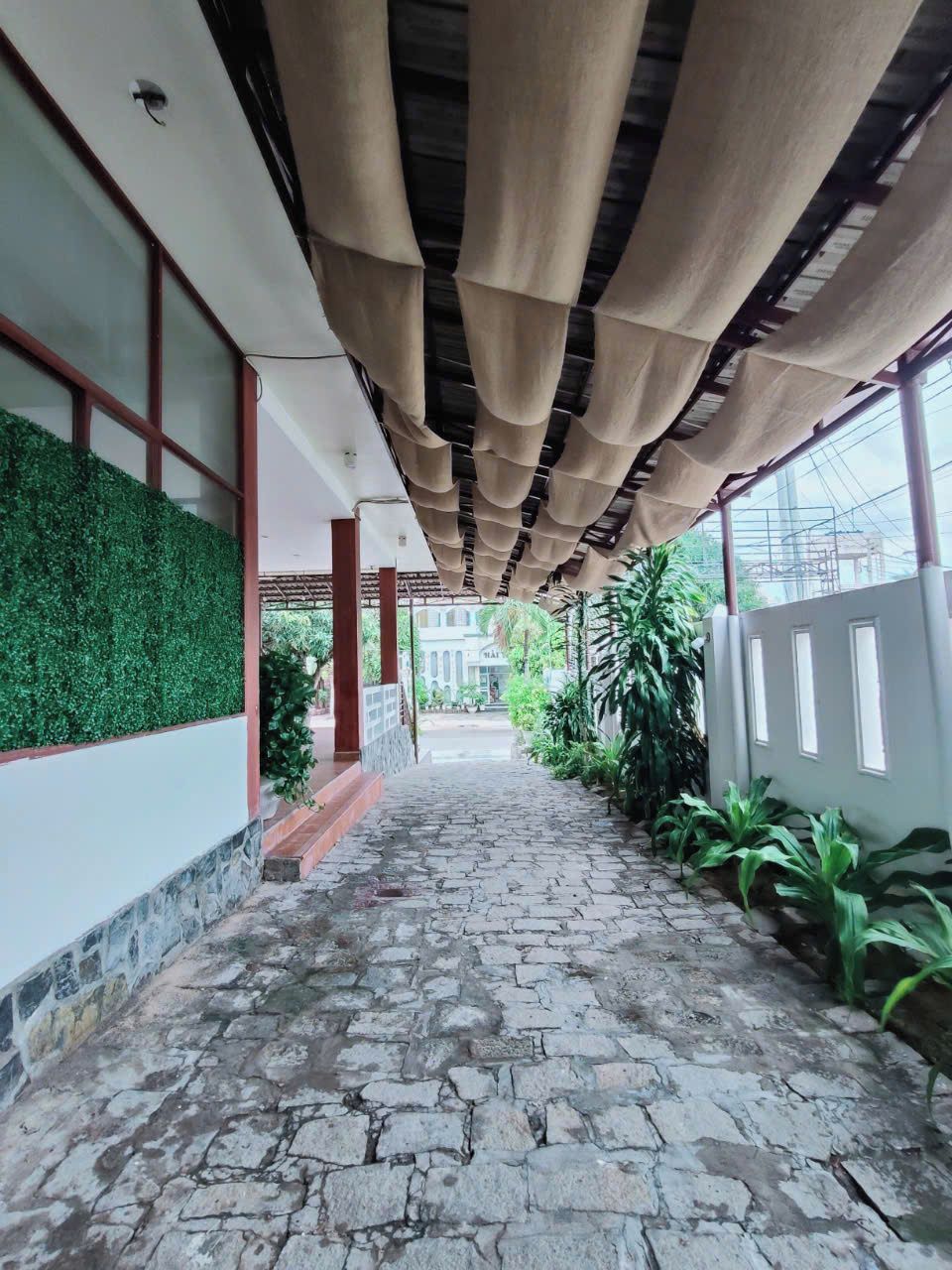 A covered walkway with stone flooring, green wall, and hanging fabric ceiling.
