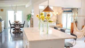 A spacious kitchen with a marble island, hanging pendant lights, and a hammock in the background.