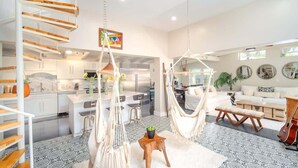 A modern interior with a spiral staircase, a hammock chair, a dining area, and a living room with a couch and a guitar.