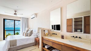 Una habitación de hotel moderna con una cama grande, un tocador con espejo y vista al océano.