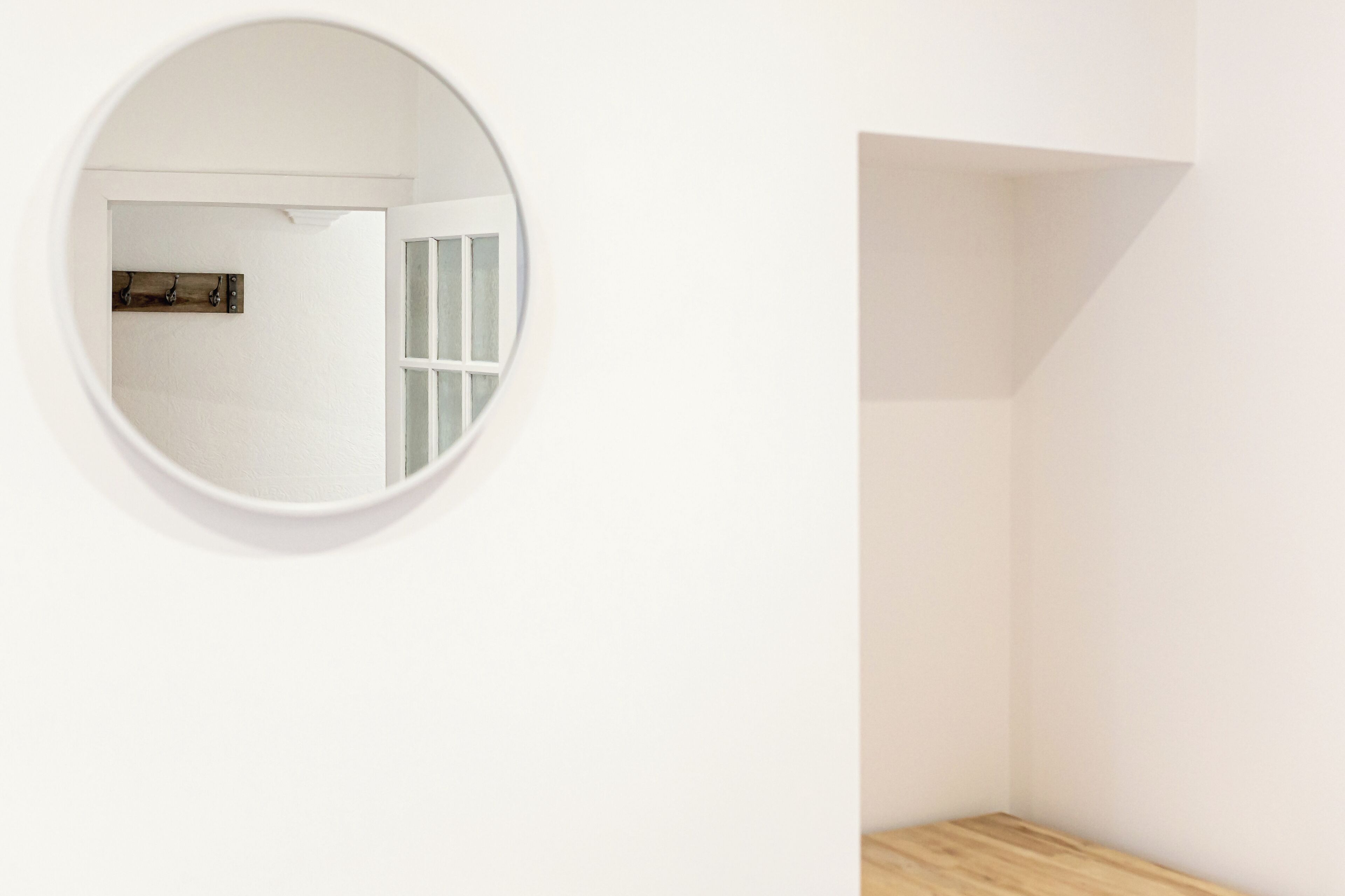 Een kamer met een ronde spiegel aan de muur, een houten vloer en een witte deur met een lichtschakelaar.