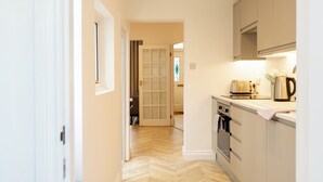 A narrow hallway leading to a kitchen with a herringbone floor pattern, a white door, and a window. - Bright & Airy 2BD - 10min walk to Centre (Cheltenham)