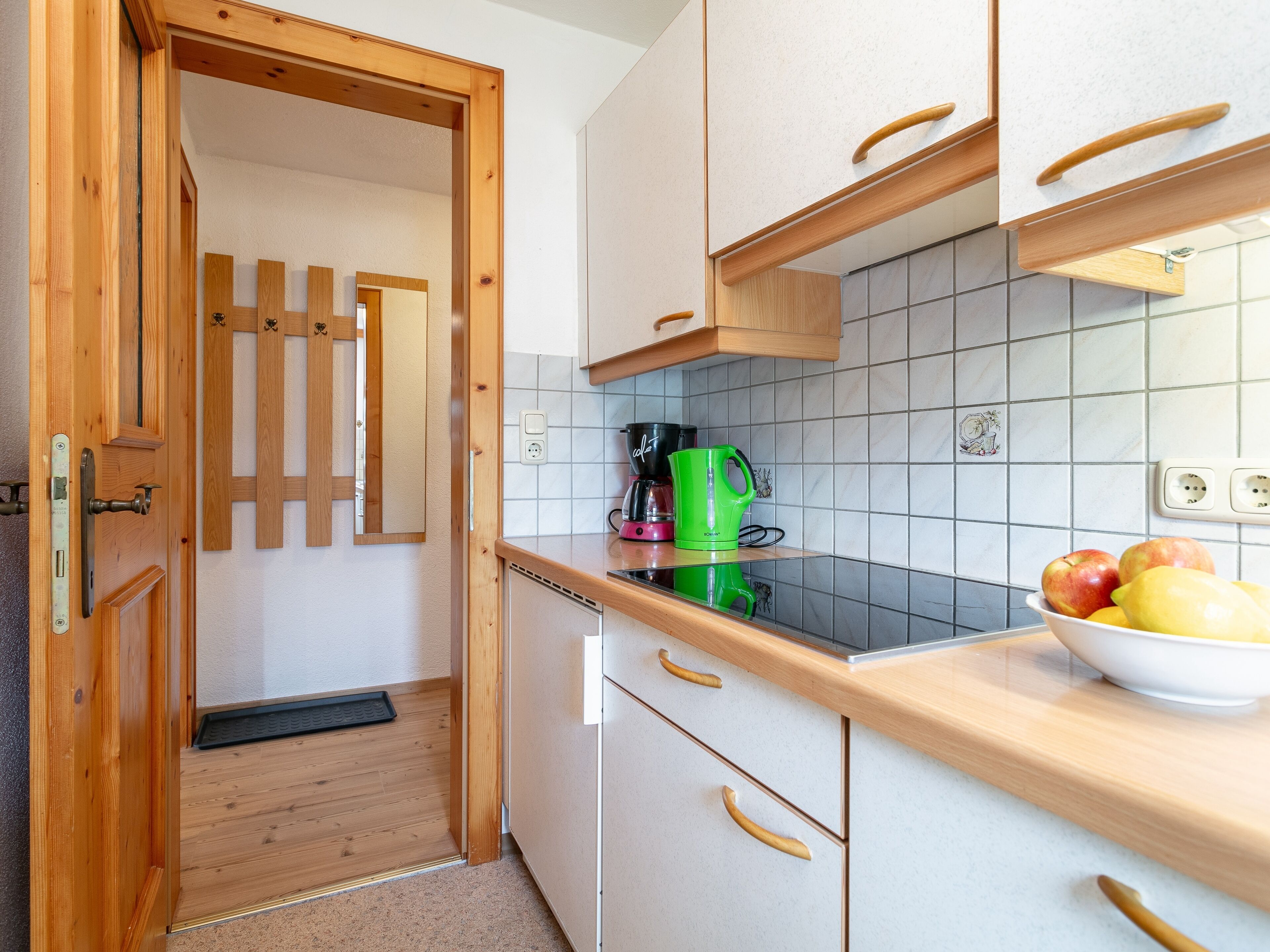 Una cocina con armarios de madera, salpicadero de azulejos y encimera con cafetera y frutero.
