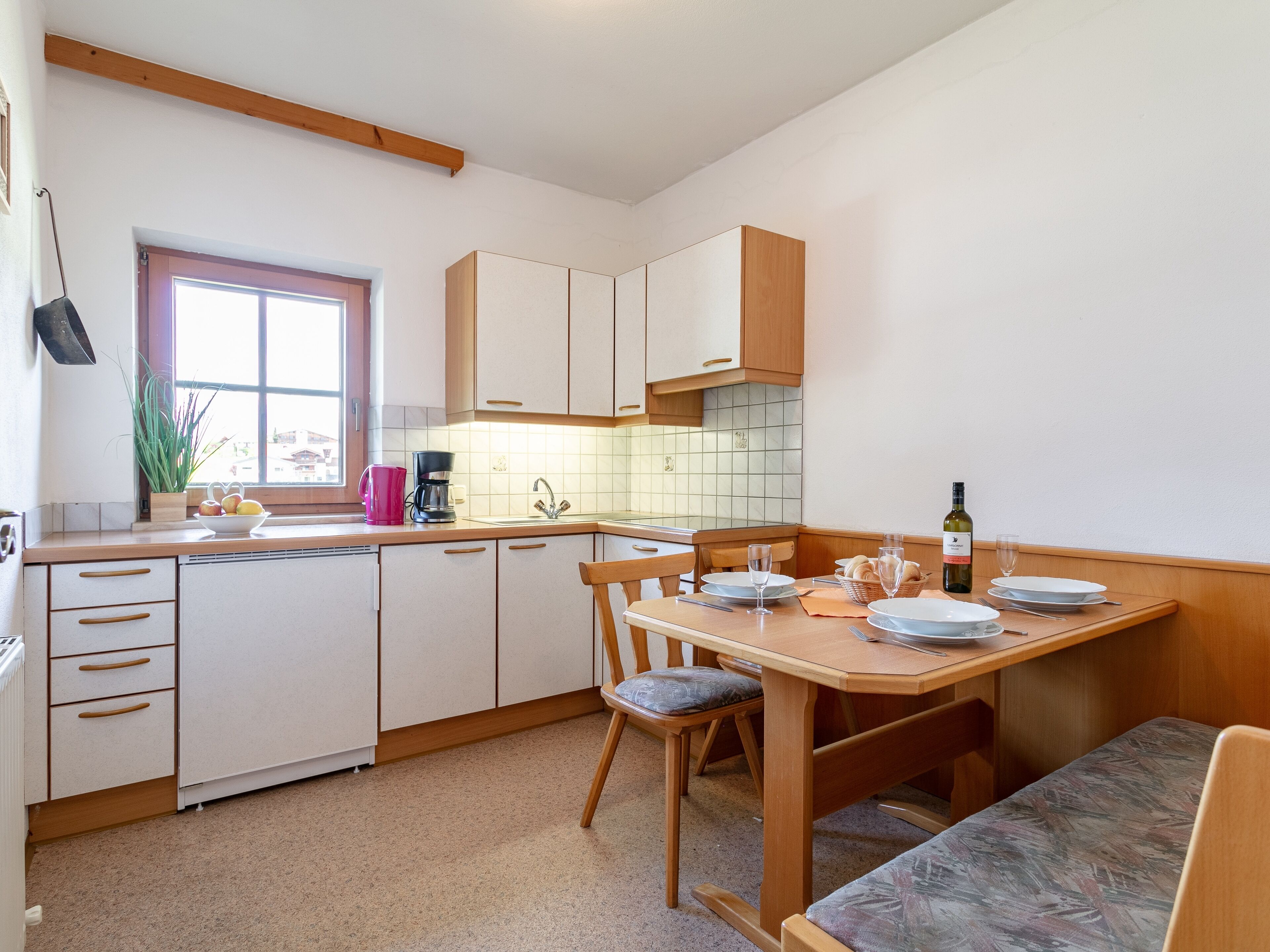 A compact kitchen with white cabinets, a wooden dining table, and a window with a view.