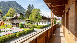 A wooden balcony overlooking a village with traditional buildings, a playground, and a mountain in the background. - Group home on a farm only 80 m from the ski bus (Reith im Alpbachtal)