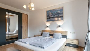 A modern bedroom with a wooden bed, bedside tables, a mirror, and a painting on the wall. - Group home on a farm only 80 m from the ski bus (Reith im Alpbachtal)