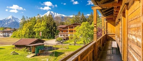 A wooden building with a balcony overlooking a green landscape and mountains.