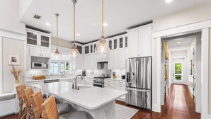 A modern kitchen with white cabinetry, a large island, stainless steel appliances, and a hardwood floor. - 3BR WaterColor Escape w/ Beach Club Access, Golf Cart, 4 Bikes & Spacious Deck for Outdoor Dining. (Santa Rosa Beach)