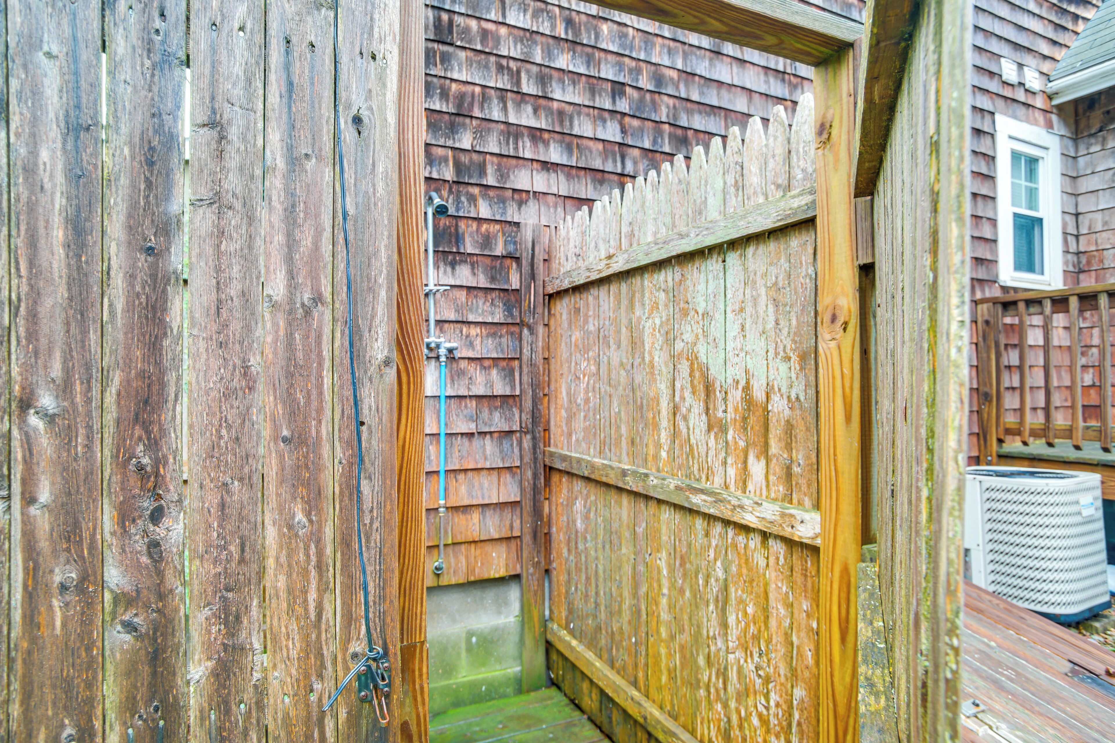 A wooden gate leading to a narrow, enclosed area with a metal pipe and a small step.