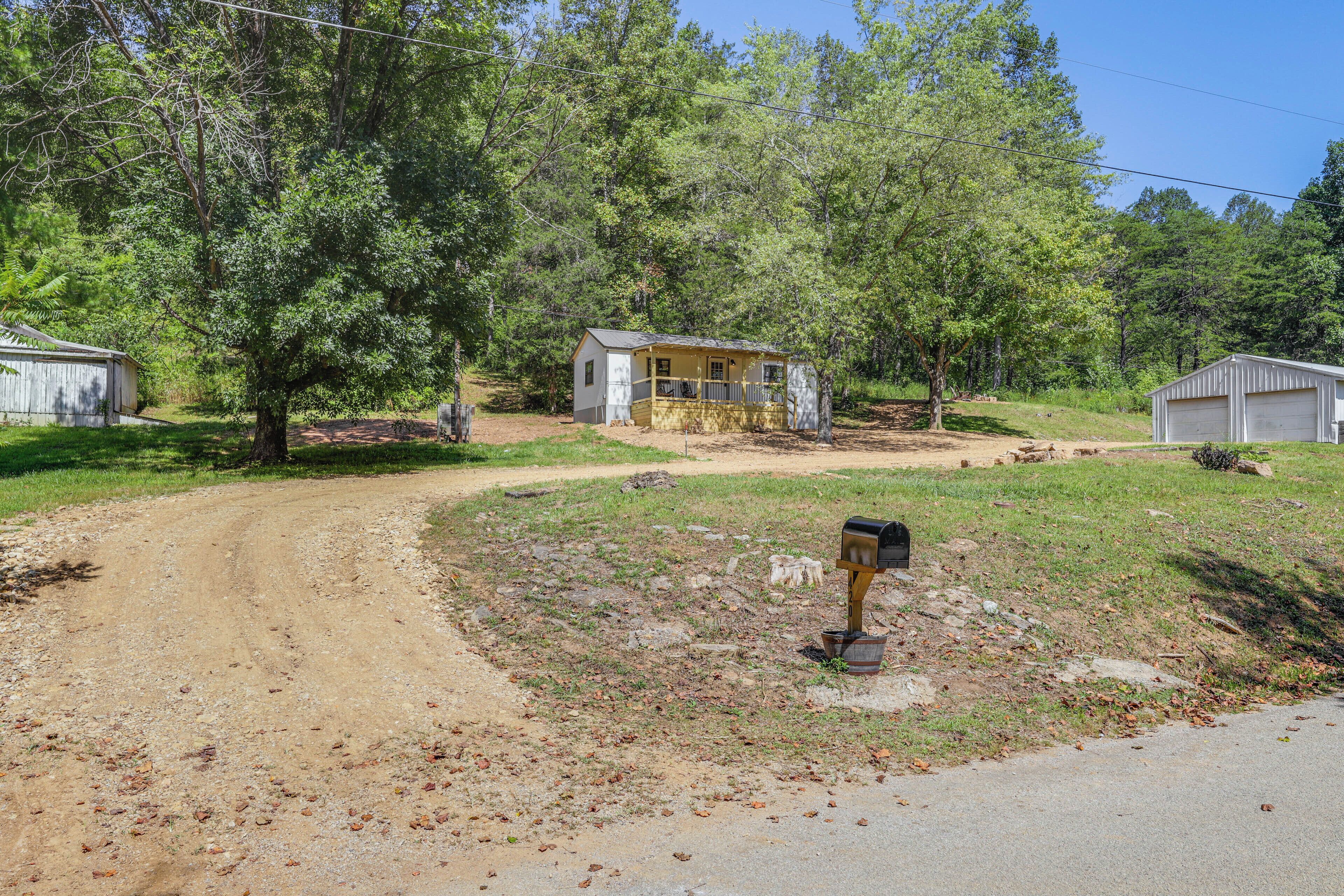 A rural setting with a dirt road, a small yellow house with a porch, and a mailbox.