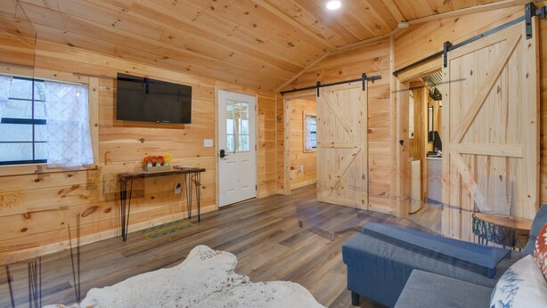 A wooden cabin interior with a sofa, a television, and a sliding barn door.