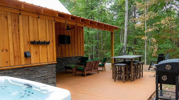 Una cabaña de madera con base de piedra, asientos exteriores, un jacuzzi y una zona de barbacoa.