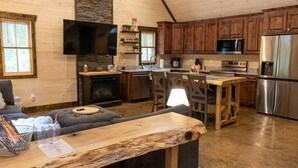 Una acogedora cocina de estilo rústico con armarios de madera, una chimenea de piedra, un televisor de pantalla plana y un comedor con mesa y sillas de madera.