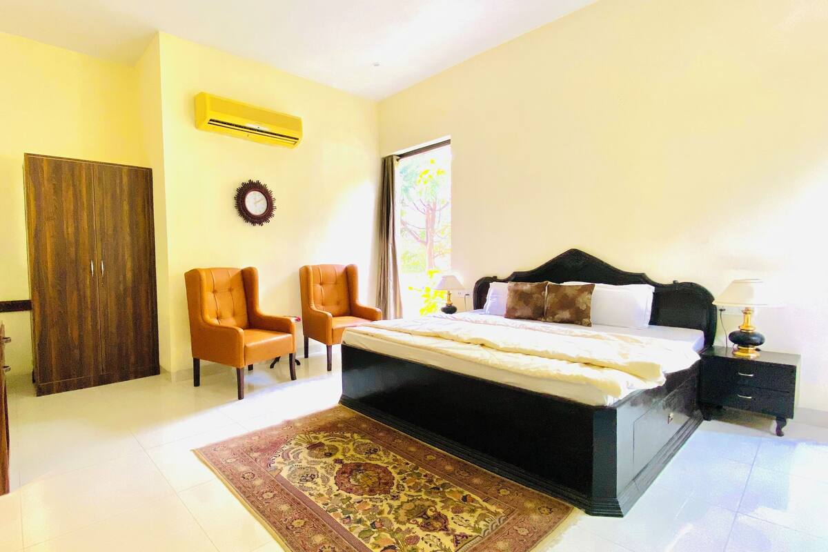 A bedroom with a bed, two chairs, a wardrobe, a nightstand, and a rug.