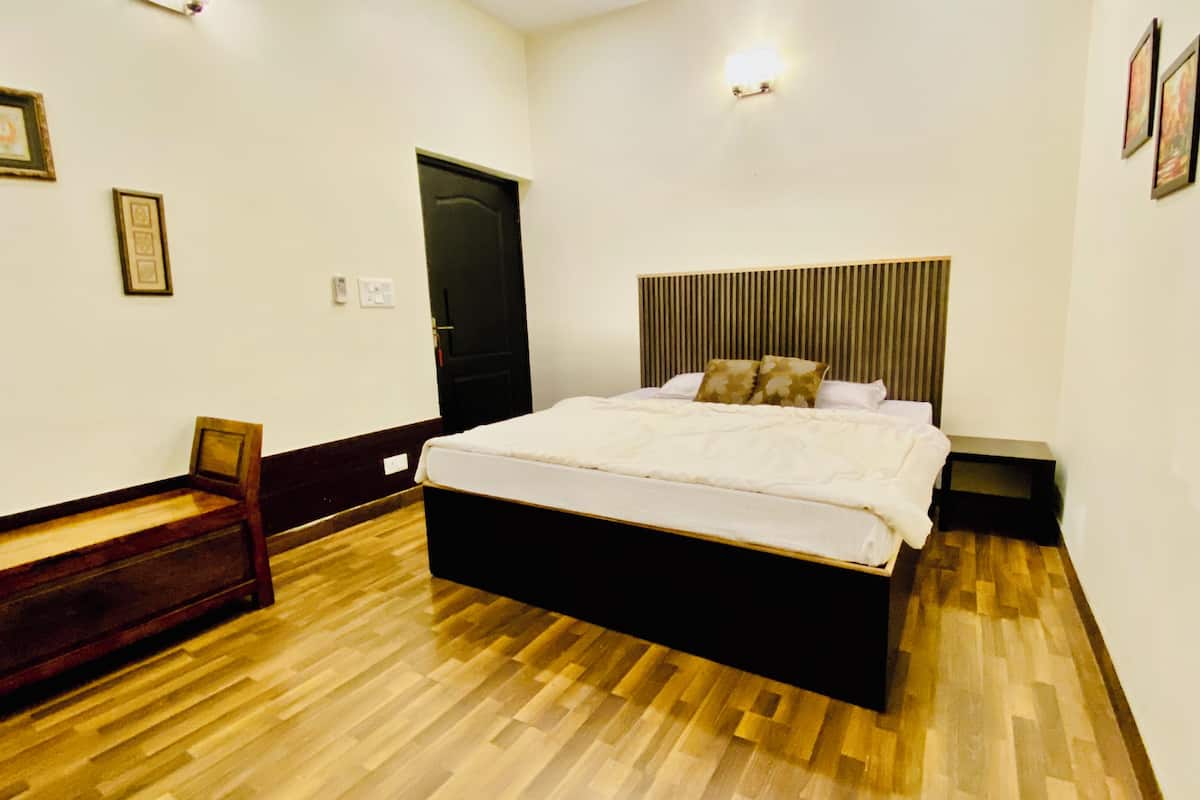 A bedroom with a wooden floor, a bed with white bedding, a headboard, and a bench by the door.
