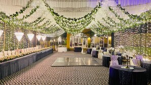 Un salón de banquetes con una larga mesa dispuesta para un evento formal, decorado con follaje y luces de adorno.