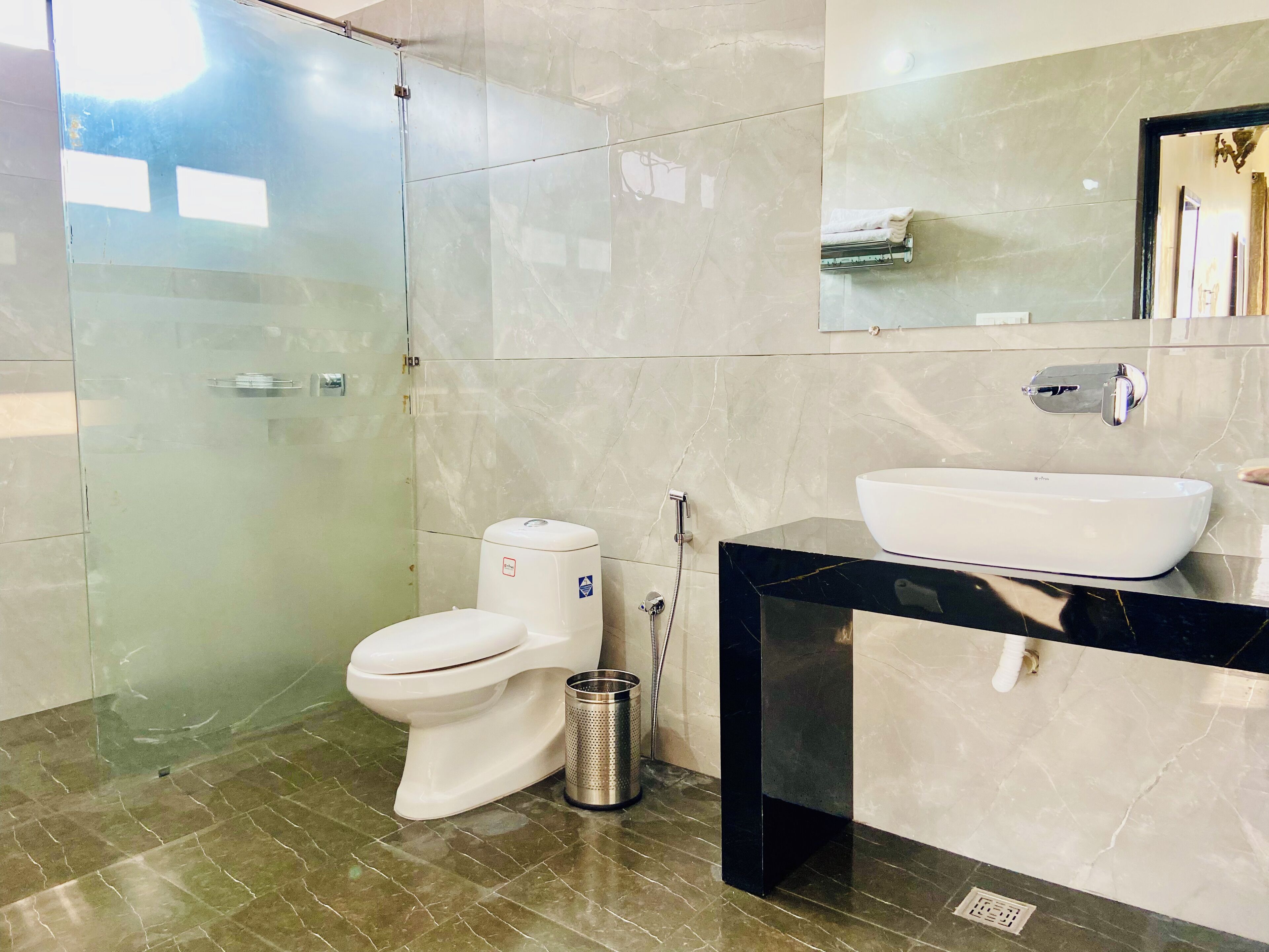 A modern bathroom with a glass-enclosed shower, a white toilet, a black vanity with a white sink, and a marble-tiled floor.