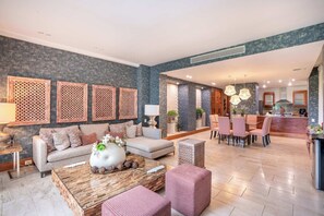 A spacious living area with a sofa, coffee table, and decorative items. There is a dining area with chairs and a table, and a kitchen in the background. - Apartment with 4 Bedrooms view in Casa de Campo (Casa De Campo)