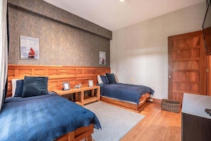A bedroom with two beds, wooden headboard, a small table, and a door. - Apartment with golf course view in Casa de Campo (Casa De Campo)
