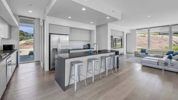 A modern kitchen with a central island, bar stools, and a large window overlooking a landscape.