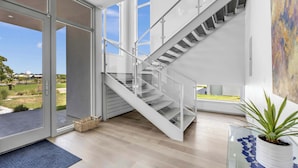 A modern interior with a glass door leading outside, a staircase with glass railings, and a potted plant on a glass table.