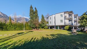 A multi-story residential building with balconies, surrounded by a well-maintained lawn and trees.