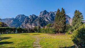 A park with a stone pathway, green grass, and a mountain backdrop.