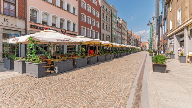 Eine gepflasterte Straße gesäumt von Außenbereich-Sitzgelegenheiten und Topfpflanzen, mit Gebäuden im klassisch europäischen Stil.