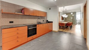 Eine moderne Küche mit orangenen Schränken, einer gemusterten Spritzschutzleiste und einem Essbereich mit einer Pendelleuchte.