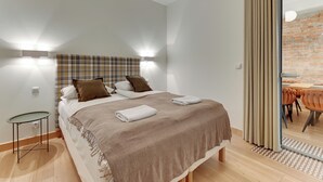 Ein modernes Schlafzimmer mit Bett, Nachttisch und Blick auf einen Essbereich durch eine Glastür.