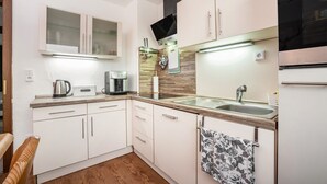 A compact kitchen with white cabinets, a stainless steel sink, a coffee maker, and a microwave. - Holiday flat ‘Fewo Trudi’ with private terrace and Wi-Fi (Waltenhofen)