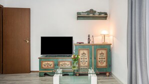 A living room with a television, a cabinet with floral designs, a vase with flowers, and a lamp. - Holiday flat ‘Fewo Trudi’ with private terrace and Wi-Fi (Waltenhofen)