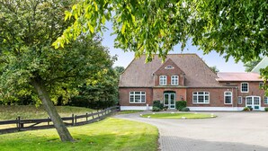 A brick building with a tiled roof, a paved driveway, and a wooden fence. - Apartment 'Deichblick' with Balcony and Wi-Fi (Wesselburenerkoog)