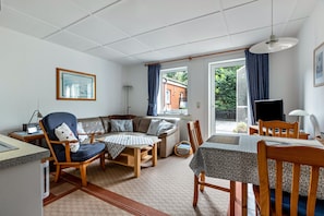 Ein Wohnzimmer mit einer Couch, einem Esstisch, Stühlen, einem Fernseher und einem Fenster mit Vorhängen.