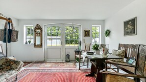 A room with a dining table, chairs, a sofa, a mirror, and a red patterned rug. - Apartment 'Deichblick' with Balcony and Wi-Fi (Wesselburenerkoog)
