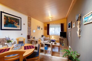 A cozy living room with a sofa, a dining table with chairs, a TV, and a bookshelf. - Failte Apartment with Scottish Charm and Wi-Fi (Selters (Taunus))