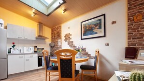Una cocina con armarios blancos, un muro de ladrillo decorativo, una mesa de comedor con sillas y un cactus sobre una mesa.