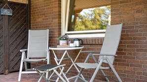 Two folding chairs, a small round table, a potted plant, and a kettle on a windowsill.