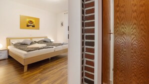 A bedroom with a wooden bed, a nightstand, a wall-mounted light, and a door with a patterned wood panel.
