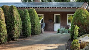 A brick house with a paved driveway, a door with the number 20, and neatly trimmed hedges.