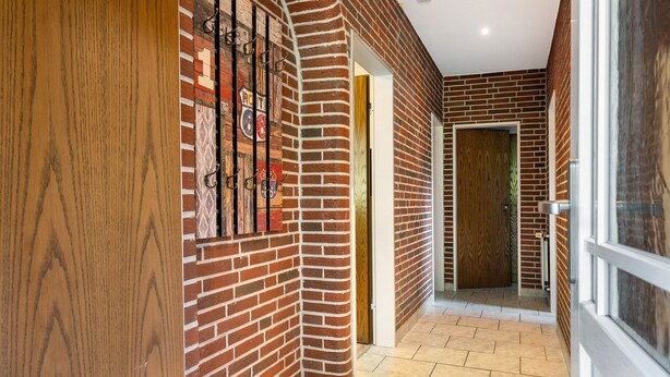 A hallway with brick walls, a wooden door, and a tiled floor.