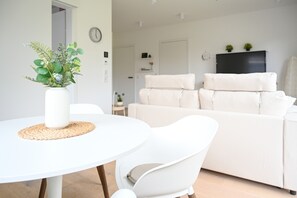 A modern living room with a white round table, a white sofa, and a television on a stand.